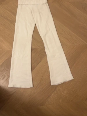 Vita stickade byxor från Gina Tricot - Säljer ett par vita stickade byxor från Gina Tricot med bred ribbad midja. Byxorna har en rak och lite vidare passform nedtill, vilket ger en chill och trendig look. Perfekta att mysa i hemma eller styla med en oversized hoodie.