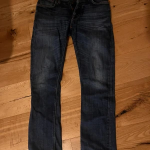 Nudie jeans  - Säljer ett par mörkblå jeans i modellen dude dan från Nudie Jeans  i storlek 30/32. Jeansen har klassisk femficksdesign, orangea sömmar och raka ben. Materialet är slitstarkt denim och passformen är normal med straight cut. Perfekt för dig som gillar stilrena och tidlösa jeans. De har ett hål mellan vänstra fick sömmen men man märker inget och hålet är väldigt minimalt! 