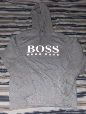 Hugoboss hoodie - Här säljer jag en hugboss hoodie, grå som är varm och skön och perfekt att stila. Stort huggmärken i mitten med lite textur om armarna och luvan