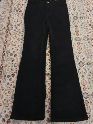 Svarta manchesterbyxor flare C 140 - Säljer ett par svarta manchesterbyxor med flare-ben från märket C i storlek 140. Byxorna har klassisk knapp och dragkedja framtill och är gjorda i mjuk manchester som ger en cool retrovibe. Perfekt för dig som gillar breda ben och vill sticka ut lite extra. 