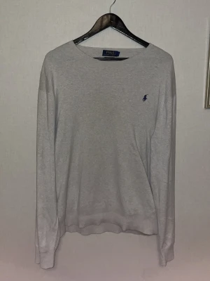  tröja Polo Ralph Lauren - Slim fit grå långärmad tröja från Polo Ralph Lauren i mjuk pima bomull. Tröjan har en klassisk rund hals och ett mörkblått broderat logomärke på bröstet. Perfekt för dig som gillar stilrena och enkla plagg med premiumkänsla.