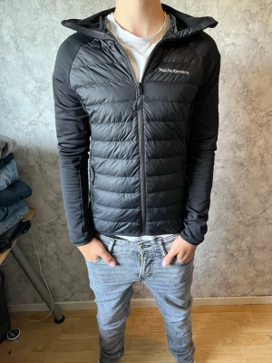Svart cardigan jacka  - Svart pufferjacka från Peak Performance i storlek S. Jackan har quiltad framsida och rygg, släta ärmar och dragkedja hela vägen. Snygg, sportig look med diskret logga på bröstet. Perfekt för kyliga dagar när du vill hålla stilen. Pris ej hugget i sten vid snabb affär. hör av dig vid minsta fundering!