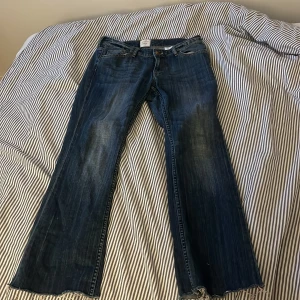 Blå bootcut jeans från L.O.G.G. - Säljer ett par klassiska blå bootcut jeans från L.O.G.G. Jeansen har råa, fransiga benslut och en snygg tvättad look. Femficksmodell med normal passform och tillverkade i slitstarkt bomullsmaterial. Perfekta för dig som gillar retrovibbar och avslappnad stil.
