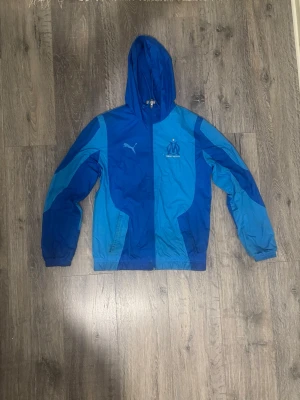Marseille windbreaker - Säljer en blå marseille windbreaker i storlek S, jackan är i bra skick men har några ljusa fläckar som man kan se på de tre sista bilderna