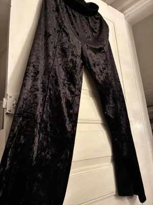 Svarta sammetsbyxor från Gina Tricot - Mörka, glansiga byxor i mjuk sammet från Gina Tricot. De har resår i midjan och ett loose, rakt snitt som ger en chill vibe. Perfekta för dig som vill ha något bekvämt men ändå snyggt. Passar till både sneakers och boots.