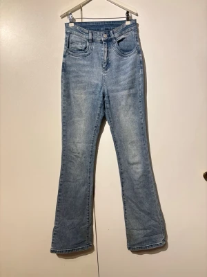 Ljusblå bootcut jeans med hög midja - Snygga ljusblå jeans med bootcut-modell och hög midja. Klassisk femficksdesign och lätt tvättad look. Perfekta för dig som gillar en retrovibe och vill ha ett par jeans som sticker ut lite extra.