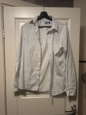 Vit skjorta med små prickar Jack & Jones - Snygg vit skjorta från Jack & Jones med små mörkblå prickar i ett diskret mönster. Klassisk krage, långärmad och knäppning framtill. Perfekt för dig som gillar stilrena detaljer och vill ha en skjorta som sticker ut lite lagom.