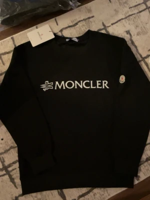 Svart Hoodie - Säljer en helt ny svart Moncler hoodie som är i storlek M men den är liten i storlek så typ S kan man säga, berätta hur mycket du väger och hur lång du är så säger jag om den passar.. Håller dig stilig och varm, om du vill köpa den vita så finns den i min profil, om det är något du undrar skriv direkt..Passa på och köp❄️