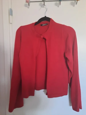 Röd kofta från Gina Tricot - Säljer en enkel och snygg röd kofta från Gina Tricot i storlek M. Koftan har rund halsringning, lång ärm och stängs med en knapp upptill. Perfekt att slänga över en topp för extra färg och värme.