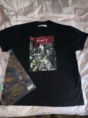 Off-white Caravaggio painting T-shirt  - Snygg off-white t-shirt köpt från Farfetch, använd 2 gånger. Det oversized fit, står att det är en M men passar mer som L-XL. Säljs på StockX för allt mellan 140-540$. Så säljer min till ett bra pris!