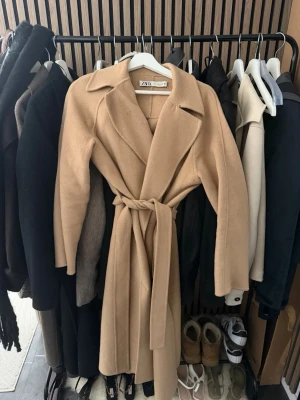 Beige lång kappa  - Beige lång kappa med knyte i midjan samt slits på vardera sida längst ner.  Köpt på Zara förra våren för 1 200kr, i storlek S. 