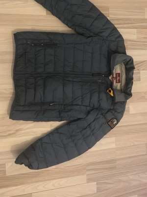 Grå dunjacka från Parajumpers - Säljer en grå dunjacka från Parajumpers med quiltad design och dragkedja framtill. Jackan har flera fickor med dragkedja och en snygg patch på ärmen. Perfekt för kyliga dagar och riktigt skön att bära. Ställ gärna frågor!
