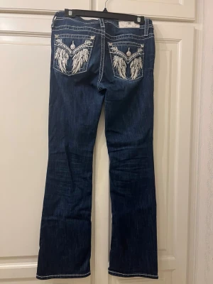 Miss Me jeans i stl 28 - Säljer mina trendiga mörkblå bootcut Miss Me jeans med vita sömmar och snygga broderade vingdetaljer på bakfickorna. 