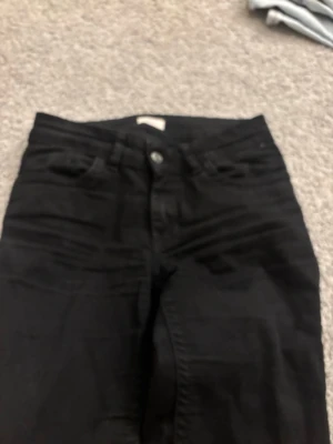 Svarta bootcut jeans från Nelly - Svarta jeans från Nelly med medel midja. Klassisk femficksdesign med snygga detaljer på bakfickorna. Jeansen har bälteshällor och knappstängning framtill. Perfekta för dig som gillar en stilren look.