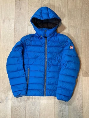 Blå Colmar pufferjacka med huva - Säljer en blå pufferjacka från Colmar med huva och dragkedja framtill. Jackan har ett quiltat mönster och två sidofickor med dragkedja. Perfekt för kyliga dagar och riktigt skön att bära. Klassisk Colmar-logga på ärmen.