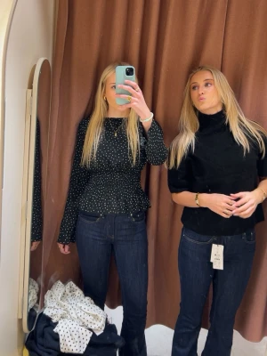 Svart prickig blus med smock - Supersöt svart blus med vita prickar och smockad midja. Långa ärmar och lätt volang nertill ger en feminin vibe. Perfekt att styla med jeans eller kjol för en trendig look.