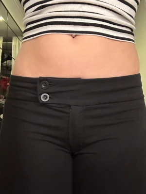 Svarta bootcut byxor från Nelly - Säljer ett par svarta bootcut byxor från Nelly i storlek S. Byxorna har låg midja, två knappar framtill och är gjorda i ett stretchigt material som sitter snyggt. Perfekta till crop tops och sneakers.