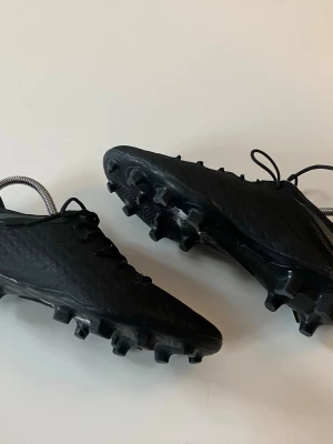 Svarta Nike Hypervenom fotbollsskor - Säljer ett par svarta Nike Hypervenom fotbollsskor med hexagonmönster på ovandelen och klassisk snörning. 