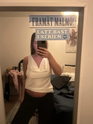 Vit omlott linnetopp med drapering - Säljer en vit ärmlös linnetopp med snygg draperad urringning och omlottkänsla. Toppen har en elegant och flowy passform som ger en stilren look. Perfekt att styla med jeans eller kostymbyxor för en trendig vibe.