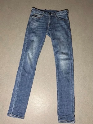Emporio Armani jeans - Säljer ett par blå jeans från Emporio Armani med klassisk femficksdesign och snygga slitningar. Jeansen har gul kontrastsöm, logga på bakfickan och patch i skinnimitation i midjan. Perfekta för dig som gillar en smal passform och stilren look.
