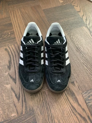 Adidas hb Spezial svarta sneakers - Säljer ett par riktigt snygga Adidas hb Spezial sneakers i svart mocka med vita detaljer och dem klassiska tre ränderna på sidorna. Skorna har snörning, brun platt sula. Adidas-logga på plös och häl. Perfekta året om. 