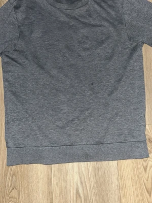 Grå slim fit tröja från BOSS - Stilren grå tröja från BOSS modell i mjukt och bekvämt material. Diskret, präglad logotyp framtill i samma färg som tyget för en clean och minimalistisk look. Passar både till vardags och avslappnad klädsel lite sliten vid armbågarna men inga hål eller nåt man tänker på 