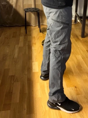 Grå cargopants från Haglöfs - Säljer ett par grå cargopants från Haglöfs med stora fickor på sidorna och dragkedja. Byxorna har justerbar snörning vid benslut och är gjorda i slitstark polyester, perfekt för äventyr och outdoor. Snygg och funktionell design med normal passform. Passar smal/medium använda men i god skick inga skador eller defekter , går att spänna fast vid fötterna finns på bild . Skick 8.5/10