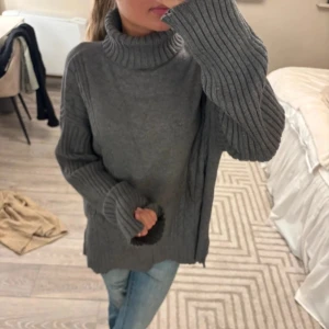 Grå stickad polotröja med ribbade ärmar - Mysig grå stickad polotröja med breda ribbade ärmar och hög krage. Tröjan har en loose fit och är perfekt för kyliga dagar. Snygg att styla med jeans eller leggings för en avslappnad vibe. Bilderna är från tjejen jag köpte tröjan av. Jag har endast använt tröjan en gång.