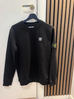 Svart sweatshirt från Stone Island - Svart långärmad sweatshirt från Stone Island med klassisk rund hals och ikonisk patch på vänster ärm. Tröjan har ribbade muddar vid ärmslut och nederkant, samt en liten logotyp på bröstet. Perfekt för dig som gillar stilrena och trendiga plagg. Kom dm för eventuella frågor 🧐pris kan diskuteras 💯