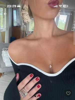 Svart offshoulder ribbad topp - Säljer en svart offshoulder topp med vit kant och ribbad struktur. Toppen har lång ärm och sitter snyggt över axlarna för en stilren look. Perfekt att styla med smycken och stora örhängen.