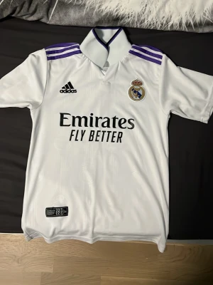 Ingen sko på bilden - Bilderna visar en vit Real Madrid matchtröja med lila detaljer, Adidas-logga och Benzema 9 på ryggen.  