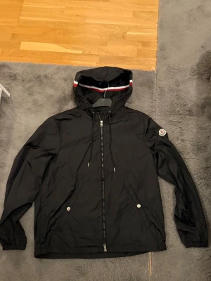 Svart Moncler vindjacka med huva - En riktigt schysst montörer vindjacka som är helt oanvänd. Säljs pga fel storlek. Storleken är 3 det motsvarar L, men sitter bra på dig som bär M. Priset kan diskuteras och hör gärna av dig vid frågor eller liknande! 