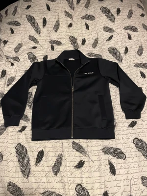 Mörkblå hoodie från Les Deux - Mörkblå hoodie Les Deux med stilren design och diskret logga på bröstet. Hoodienhar ribbade muddar, ståkrage och två sidofickor. Materialet är mjukt och slätt, med hel dragkedja framtill. Perfekt för dig som gillar minimalistisk och clean stil.