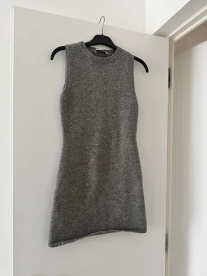 Grå ärmlös stickad klänning från Zara - Säljer en grå stickad klänning från Zara i storlek S. Modellen är ärmlös med rund hals och har en slim passform som sitter snyggt mot kroppen. Materialet är mjukt och skönt stickat.
