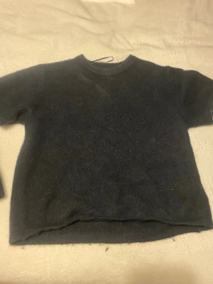 Mörkblå stickad tröja med kort ärm - Säljer en enkel och stilren mörkblå stickad tröja med korta ärmar och rund hals. Perfekt att matcha med jeans eller kjol för en chill look. Materialet är mjukt och ger en skön känsla mot huden.