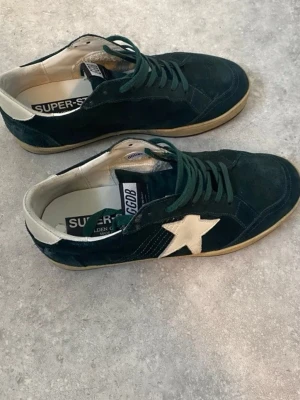 Golden Goose - Säljer ett par gröna mocka golden goose ball star sneakers. Skorna är i bra skicka inga defekter osv bara smutsiga (Skicka 7,5/10). Storlek 42 box ingår, skriv vid minsta fundering eller vid behov av fler bilder. Kan gå ner i pris vid snabb affär.