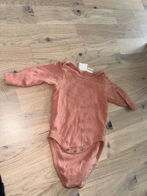 Zara rosa body, storlek 62 Rostfärgad body från Zara 1-3 mån - Supersöt rostfärgad body från Zara i mjuk bomull. Modellen har långa ärmar och tryckknappar i grenen för enkel påklädning. Perfekt basplagg för de allra minsta.Långärmad body i en enfärgad design med tryckknappar i grenen.