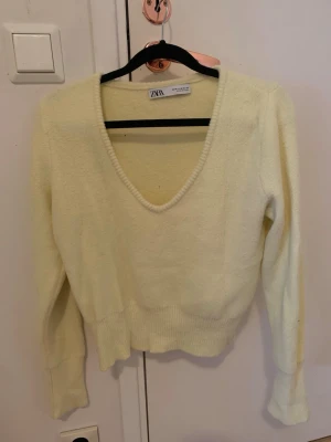 stickad tröja  - Supermjuk ljusgul stickad tröja från Zara med djup v-ringning och ribbade muddar vid ärmslut och midja. Tröjan har lång ärm och en lite croppad passform som sitter snyggt till jeans eller kjol. Perfekt för dig som gillar stilrena och ljusa färger.