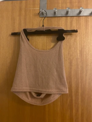 Beige ribbad croppad linnetopp - Säljer en beige croppad linnetopp från SHEIN i storlek M men passar även mindre strl. Toppen är ribbad och har en ärmlös design med rundad hals och öppen rygg. Perfekt för varma dagar och enkel att matcha med jeans eller kjol.
