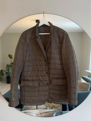 Oscar Jacobsson kavajjacka - strl 50/M - Quiltad kavajjacka i mörkbrun färg med klassisk krage och tre knappar framtill. Jackan har två stora fickor med lock och är långärmad. Materialet är syntet och ger en lätt och smidig känsla. Perfekt för dig som gillar stilren och modern look.