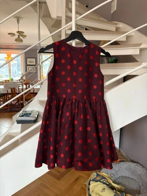 Prickig klänning storlek 134 Arket  - Säljer en vinröd kortklänning med röda prickar. Klänningen är ärmlös och har en rund halsringning samt ett utställt kjolparti som ger en skön och lekfull siluett. Perfekt för dig som gillar färg och mönster.
