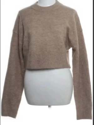 Beige croppad stickad tröja från Zara - Säljer en beige croppad stickad tröja från Zara med rund hals och långa ärmar. Tröjan har en loose passform och är perfekt för lager-på-lager under hösten och vintern. Enkel och stilren design som funkar till många olika outfits.