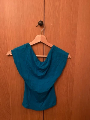 Blå topp med djup rygg från SHEIN - Snygg blå topp från SHEIN med draperad halsringning och öppen rygg. Toppen är nästintill ärmlös och har en figurnära passform som framhäver siluetten. Perfekt att styla med jeans eller kjol för en trendig look.