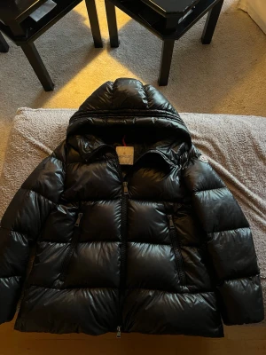 Svart Moncler pufferjacka med huva - Moncler Seritte Giubbotto down jacket i strl 3. Nypris ligger på 17100kr. Jätte bra skick och sparsamt använd, utan några defekter. Lte missfärgning på dragkedjan kan förekomma, men absolut inget man märker av om man inte kollar efter extremt noggrant! Köpt på NK i Göteborg 2021. Perfekt nu i vinter🤩Skriv privat för mer bilder och info. Självfallet äkta.