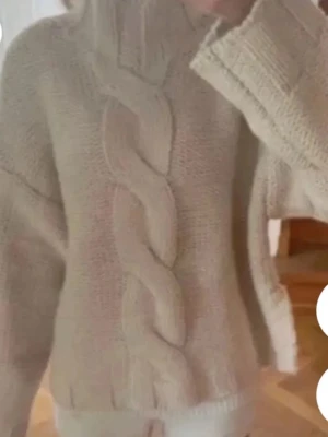 Beige stickad tröja Zara  - Säljer en beige stickad tröja med grovt flätmönster framtill och hög krage. Tröjan har långärmade och ribbade muddar vid ärmslut och nederkant. 