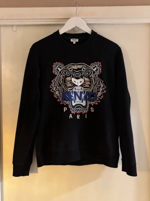 Svart Kenzo sweatshirt - Svart sweatshirt från Kenzo med ikonisk broderad tiger och logga på bröstet. Perfekt för dig som vill sticka ut med en cool design. Tröjan är i fint skick. Hör av er vid funderingar!