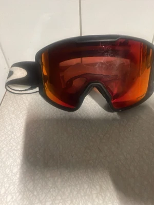 Oakley skidglasögon  - Skid-/snowboardglasögon i vitt 🤍 Spegelglas (röd/orange ton) som skyddar bra mot sol och bländning. Sitter bekvämt och stadigt, justerbart band. Använda – finns repor på glaset (se bild), därav priset. Perfekta som extra par eller för nybörjare ⛷️🏂 Pris kan även diskuteras 