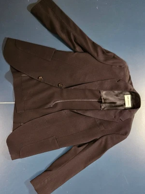 Mörkblå kavaj från Our Legacy - Säljer en mörkblå kavaj från Our Legacy i klassisk modell med två knappar framtill och fickor med lock. Kavajen har slimmad passform och är tillverkad i ett mjukt tyg med slät yta. Perfekt för dig som vill ha en stilren och tidlös look.