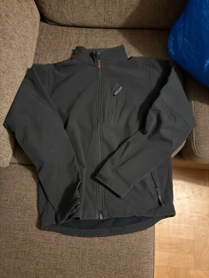 Svart vindjacka från Didriksons - Säljer en svart vindjacka från Didriksons med hög krage och flera praktiska fickor med dragkedja. Jackan har en clean look, hel dragkedja framtill och justerbara ärmslut med kardborre. Perfekt för blåsiga dagar och enkel att matcha.