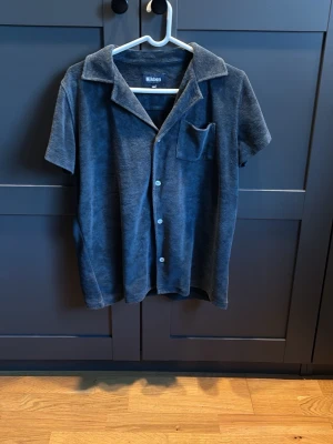 Mörkblå frottéskjorta från Nikben - Säljer en mörkblå skjorta från Nikben i mjuk frotté. Skjortan har korta ärmar, klassisk krage, bröstficka och knappar framtill. Perfekt för chill dagar och har en loose passform som ger en avslappnad vibe.